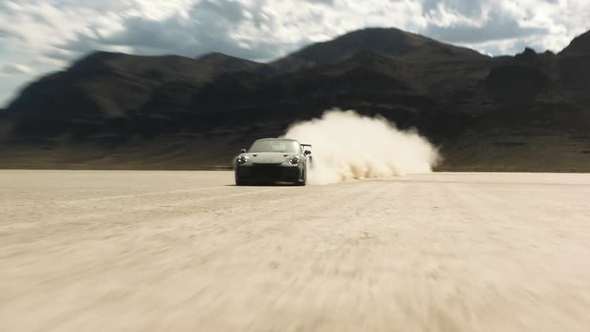 A black sports car driving through the desert kicking up think dust behind it