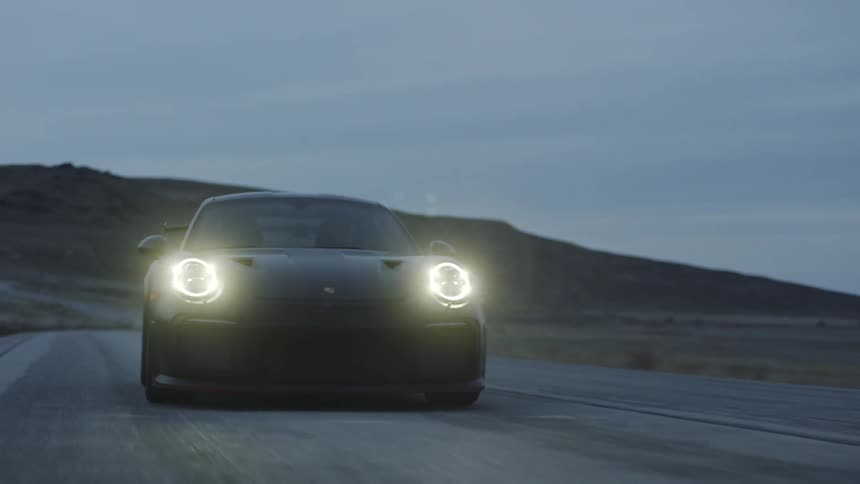 A black sports car driving down the road at dusk with the headlights on