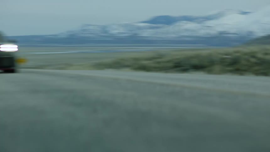 Black sports car drives on country road with green hills and snowy mountains in the background