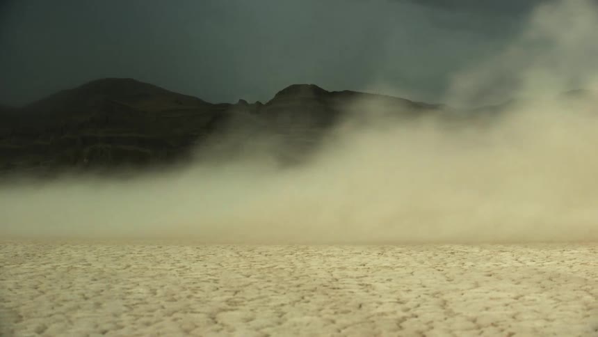 A black coupe sports car driving around in the desert with mountain ranges in the background