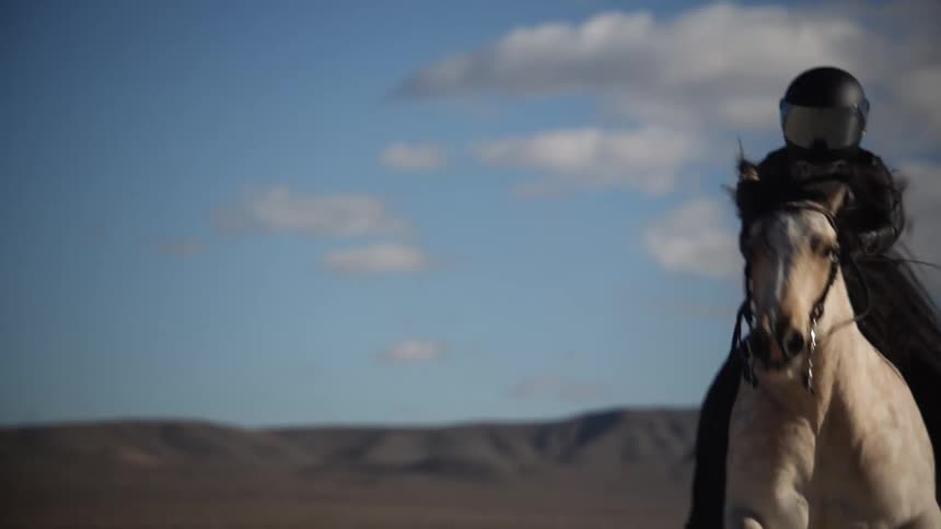 A person wearing all black riding a tan horse through the desert