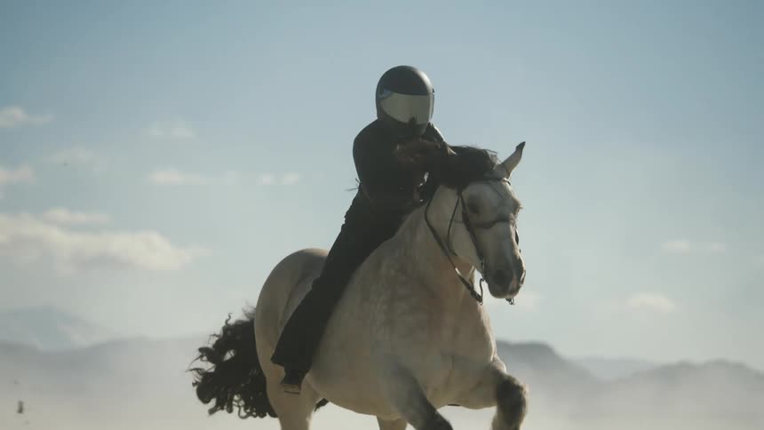 Woman wearing black helmet leather jacket and pants rides horse in the desert