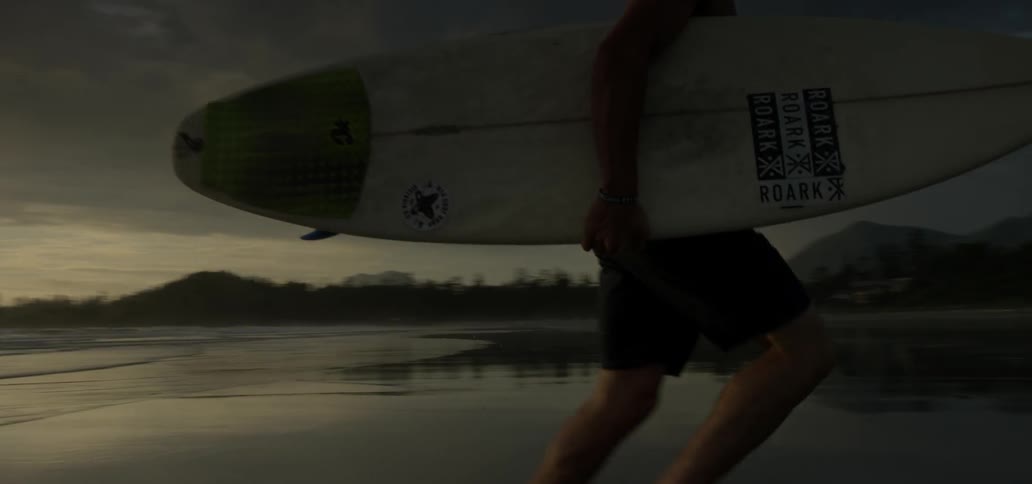 A man running away from the water while carrying a surfboard as the sun sets at the beach