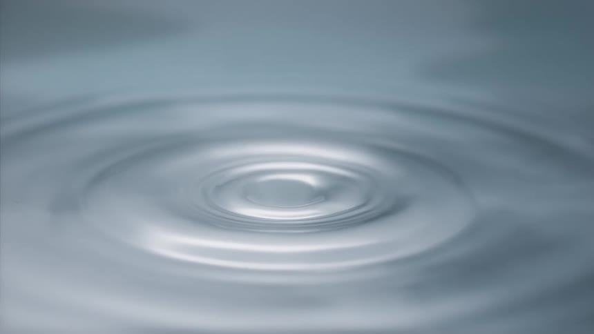 Water drop splashes into pool of water splashing up and creating concentric circles