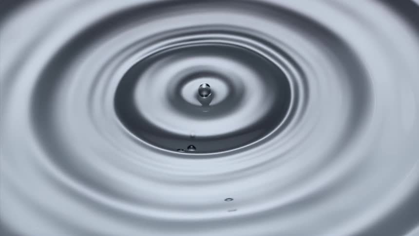 Water drop falling on the calm water surface creating circular ring waves and ripples