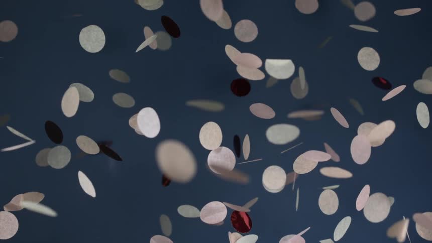 Paper and rose gold paper confetti falling from above across a blue wall