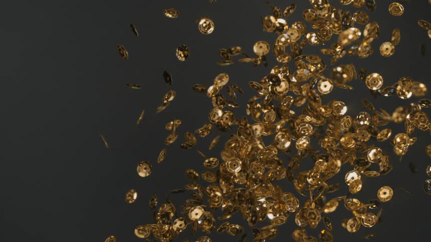 A handful of gold sequins are thrown into the air in slow motion