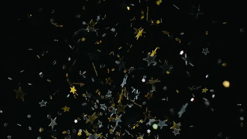 Confetti with stars are being thrown into air on the black background