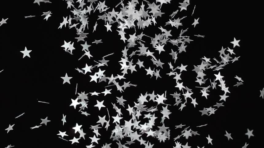 White star shaped cutouts are tossed into the air against a black background and slowly fall