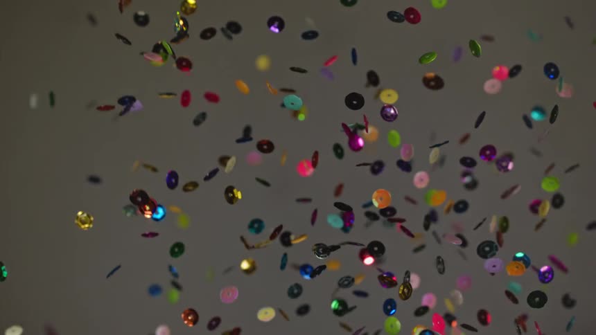 A bunch of rainbow sequins are thrown into the air and fall in slow motion
