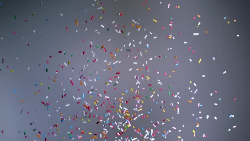 Rainbow sprinkles are thrown into the air and fall in slow motion