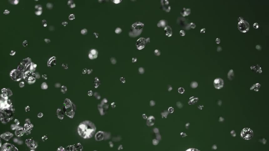 Glass diamonds scattering all over a green background in slow motion