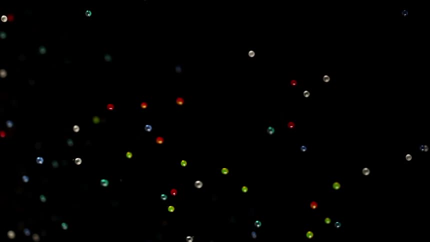Light is reflecting on small colored spheres as they float in the darkness