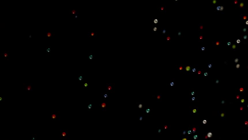Light is reflecting on small colored spheres as they float in the darkness