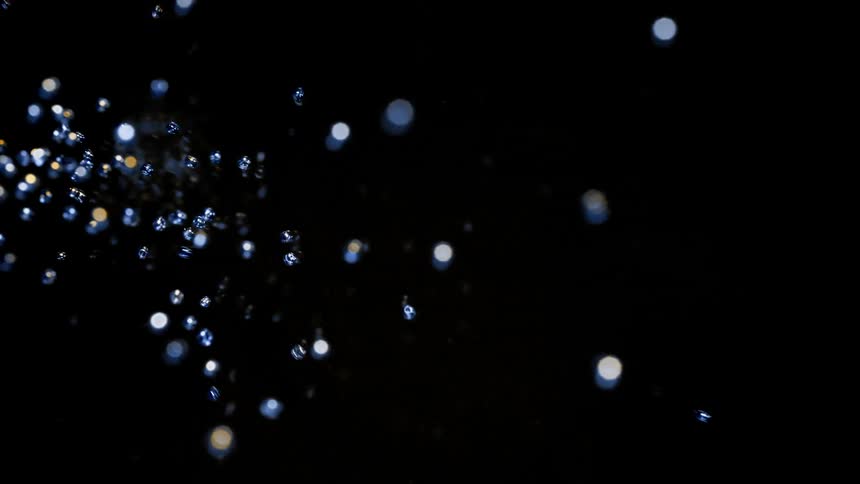 Blue pearls spread colliding with each other and flowing across black background as they form spots of light glare