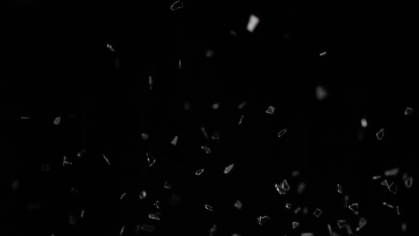 Small pieces and shiny shards reflect light as they fly in the darkness in slow motion