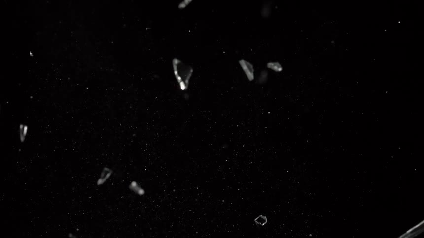 Glass shards fly into the air then fall through the darkness