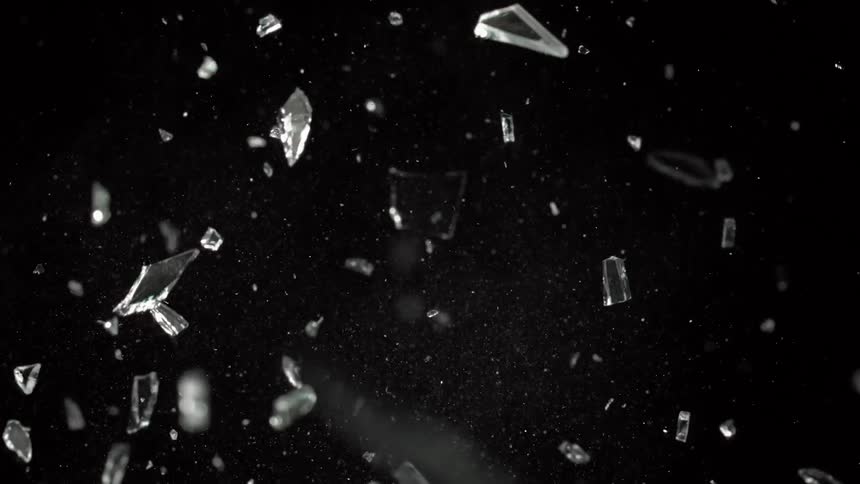 Shards of glass fly into air then fall leaving powdered bits floating against black background