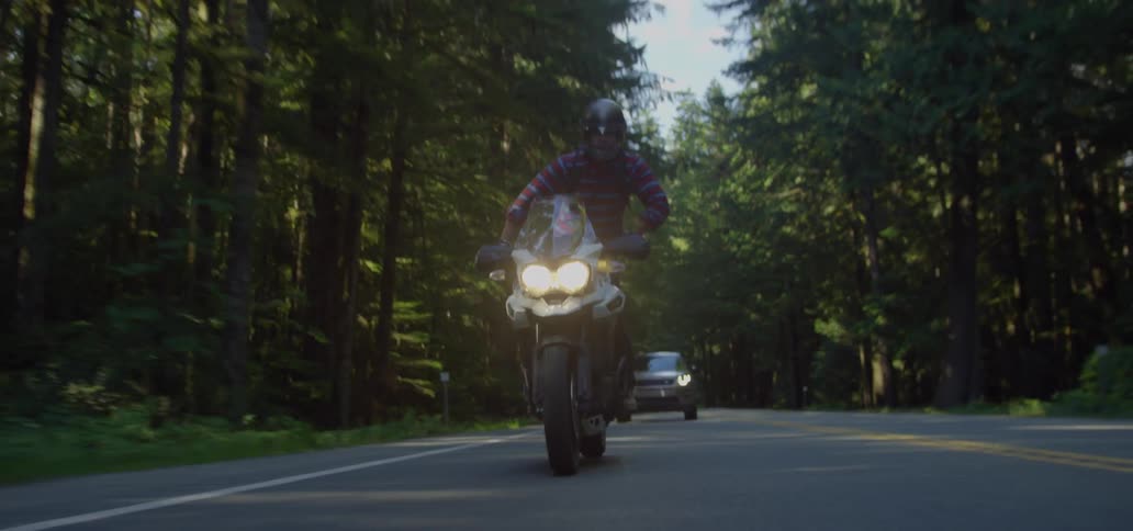 Motorcyclist driving on a paved road with a car not far behind