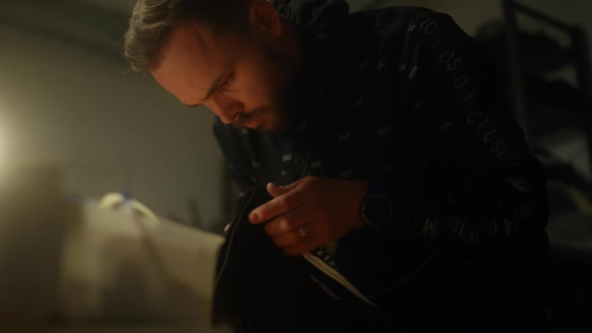 Male tailor with beard and leather jacket folds clothes in tailors store