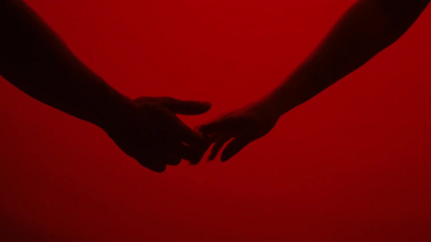 A woman and a man pass each other walking and they reach out their hands and touch