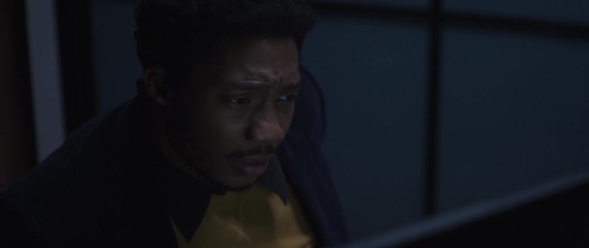A man is sitting at a desk looking at a computer screen and he appears to be confused and disturbed as his hands move to the keyboard