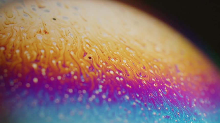 Fluorescent colors move across the surface of a sphere and blend as small orbs float over the surface pulling a trail of color with them