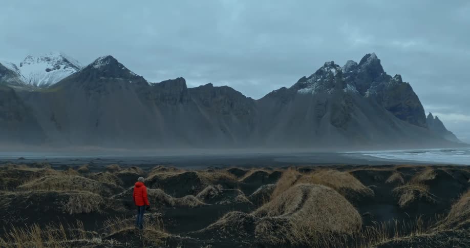 A person stands in front of a mountain range and looks at the view
