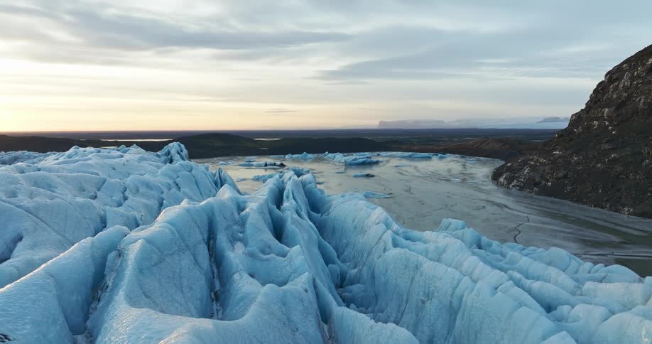 Frozen snow covered ridges stand along a frozen lake near a mountain under a cloudy sky