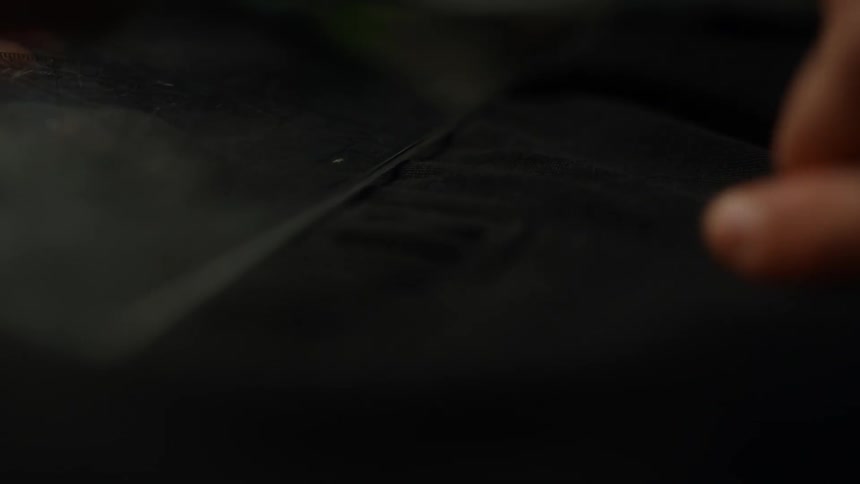 A persons finger moves over a dark surface as they pick up a shiny glass object