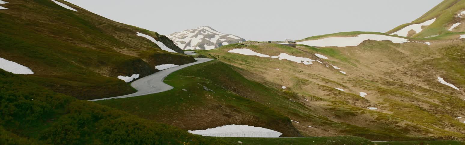 A narrow road curves through snow capped hills and mountains