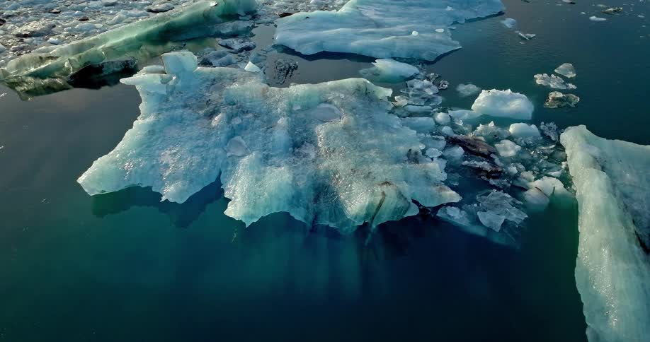 Ice and icebergs float on still reflective waters all tinted blue green