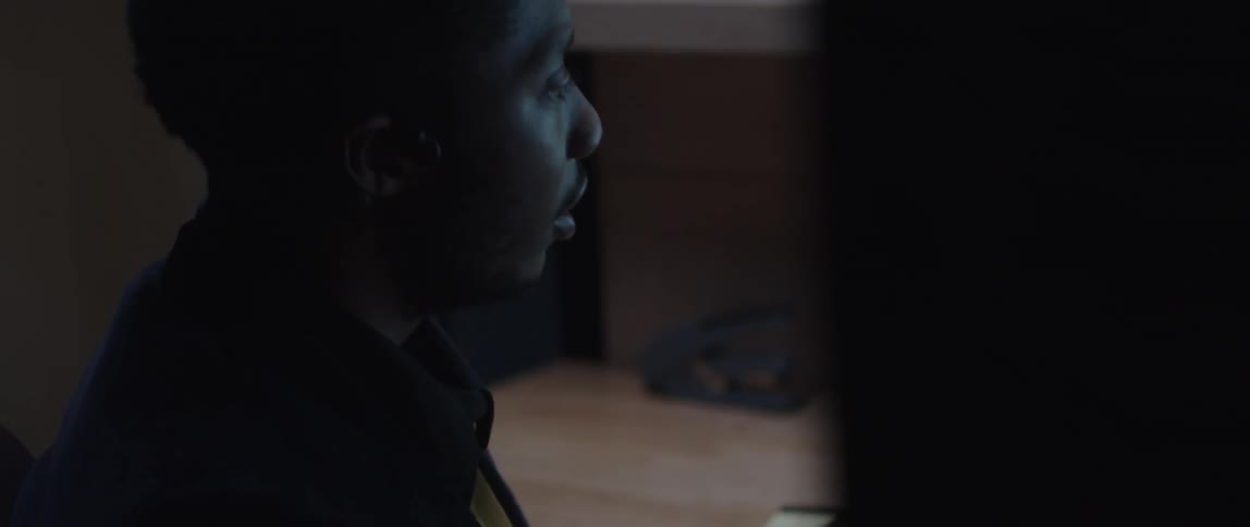 Man wearing black coat sits in chair talking in room