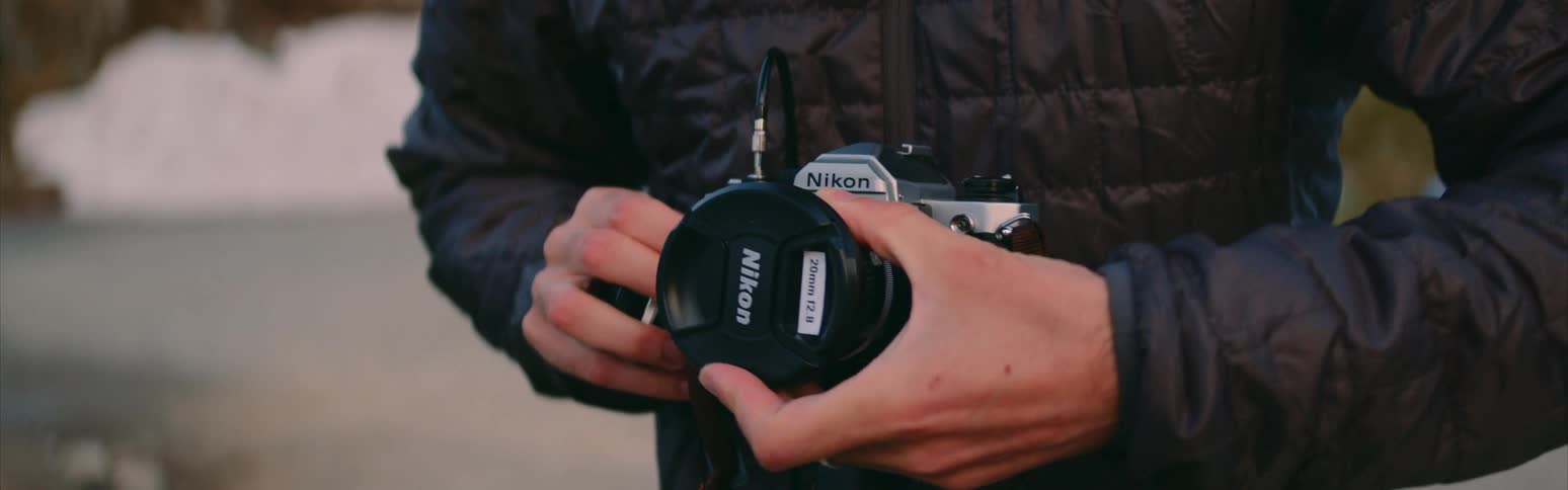 A photographer is changing the lens on a nikon camera as it sits on a tripod