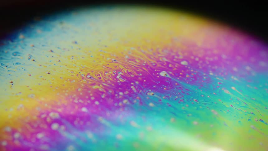 Fluorescent colors move across the surface of a sphere and blend as small orbs float over the surface pulling a trail of color with them