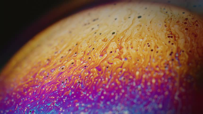 Fluorescent colors move across the surface of a sphere and blend as small orbs float over the surface and the color moves down