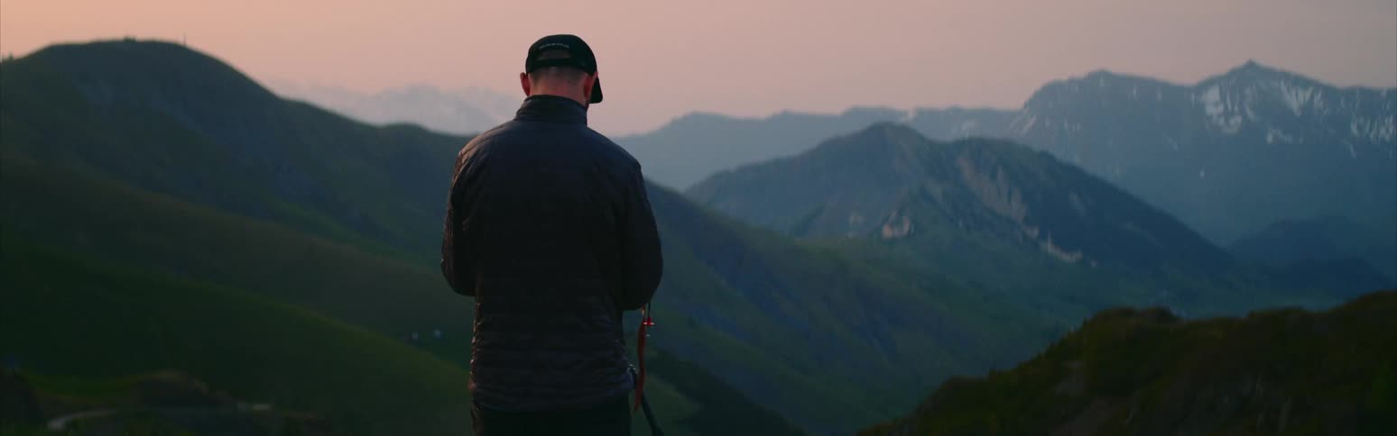 Male photographer adjusts camera on tripod set overlooking foggy mountains and valley under a red sky