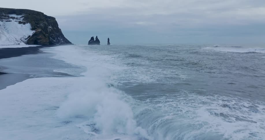 Waves roll onto beach with outcropping sitting near snow covered promontory