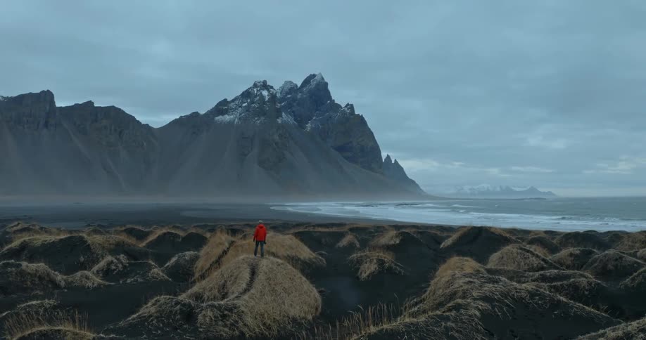 A person in a red coat looking out toward the coast and mountain