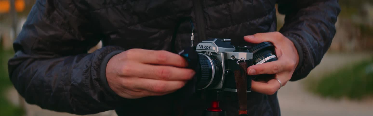 Man in black coat cleans camera lens on tripod in the field