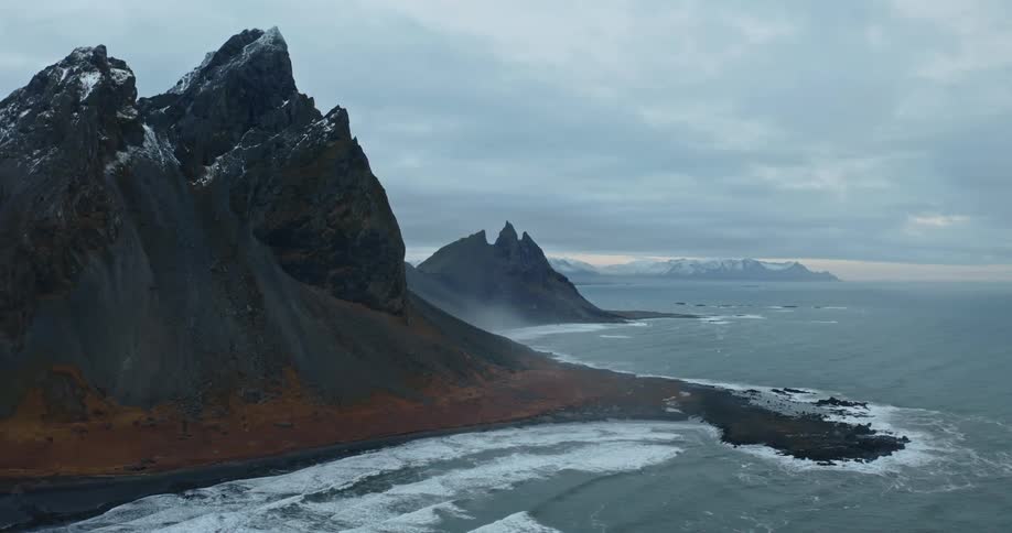 Waves crash onto the shore below snow capped mountains