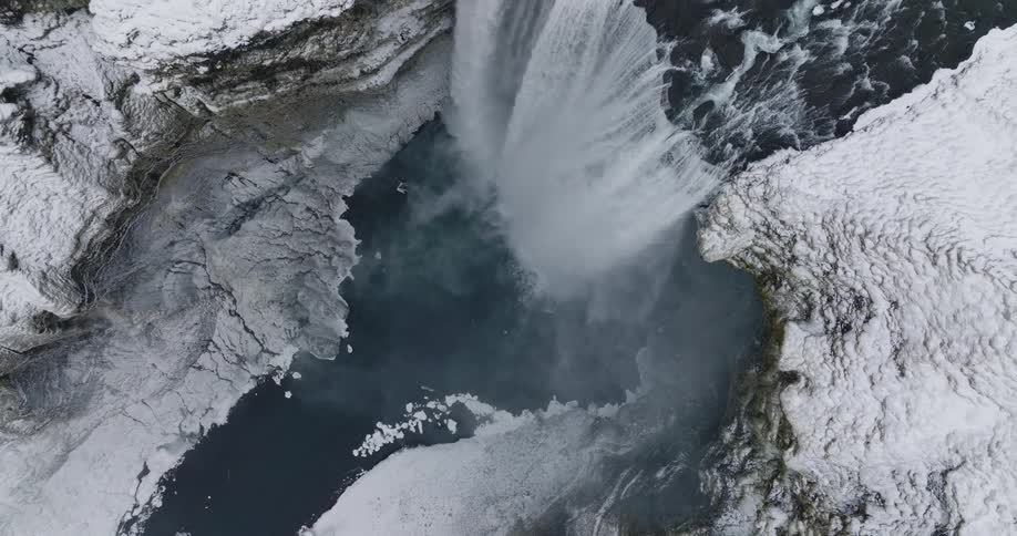 An aerial view of a waterfall flowing over an icy cliff in the wilderness