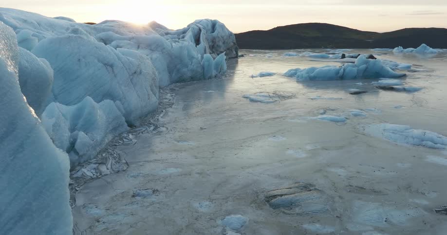 Sunshines across glacier towering over frozen water doted with icebergs