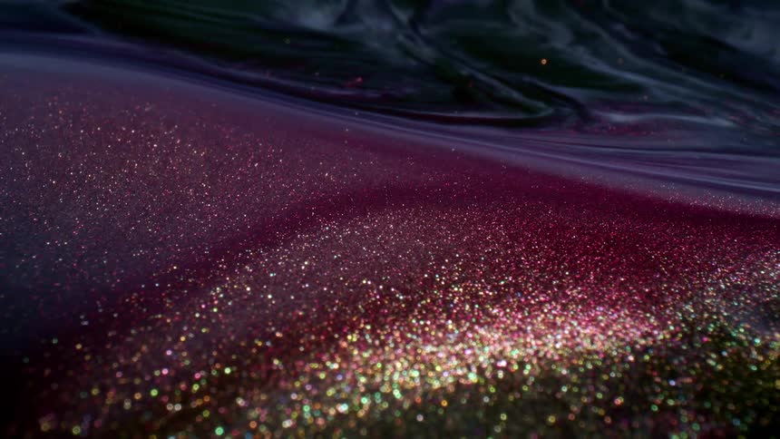 A fluid with a purple hue and shimmering golden glitter suspended in it flows around and swirls