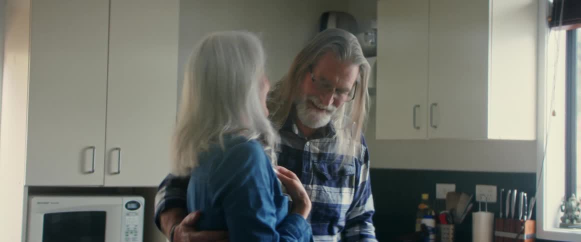 Older couple smiles and hugs while standing in kitchen