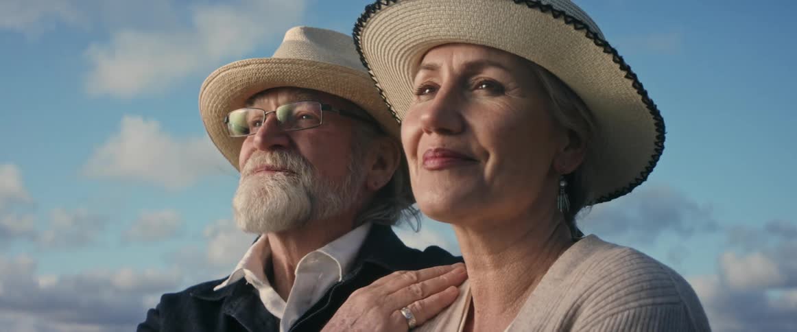 An elderly man rubs a womans shoulder as they smile outside