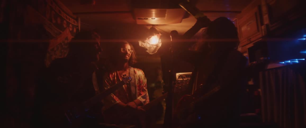 Musicians in dimly lit cramped area watch one of the guitarist drink from the bottle