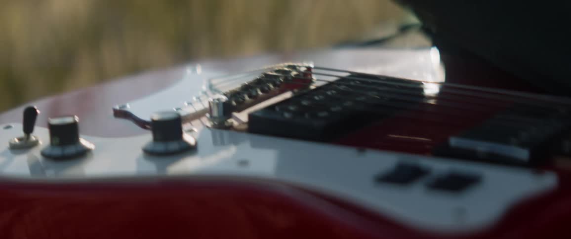 A person outside runs their hand over a guitar