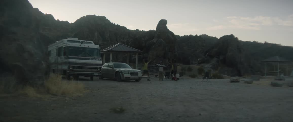 A group of people hold up their hands and then hug each other near a car and an rv
