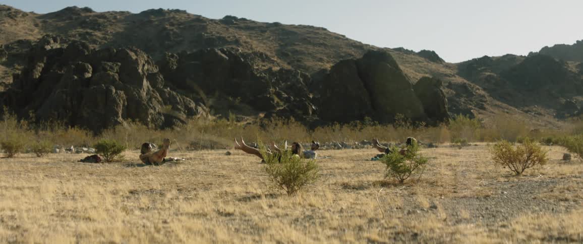 People do yoga in a field in front of a mountain range